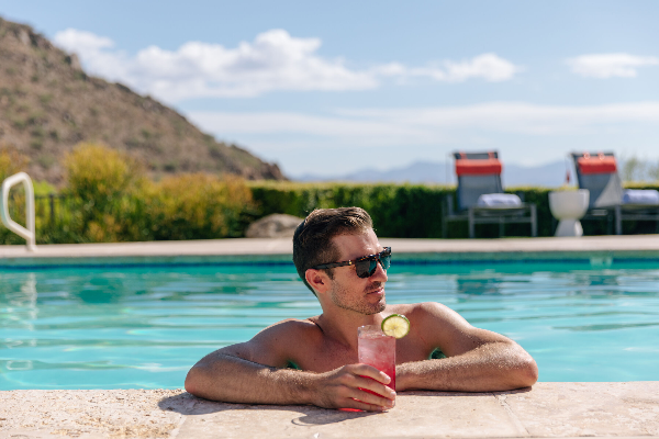 man lounging in pool with drink in hand